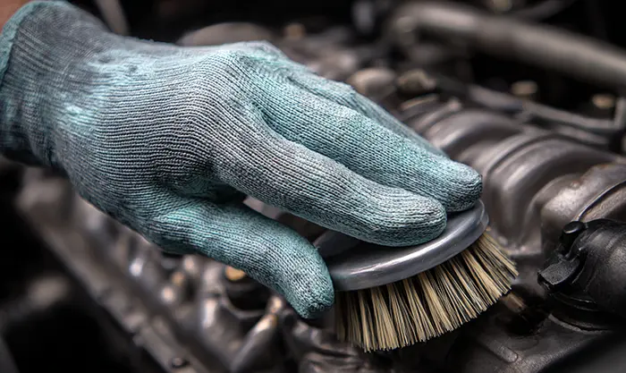 Main gantée appliquant un dégraissant avec brosse douce sur moteur