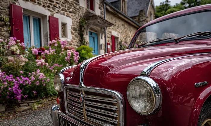 Renault 4 rouge vintage devant une maison de village, détails de carrosserie
