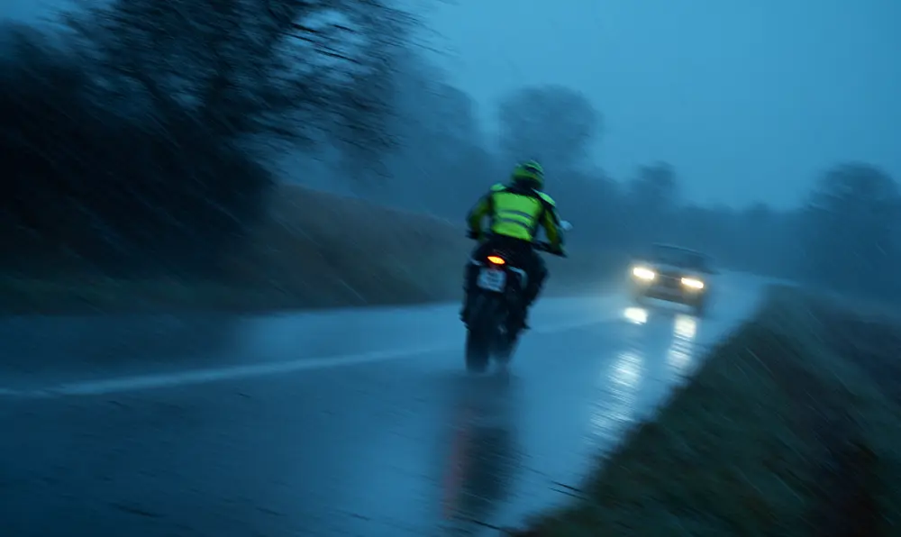 motard silhouetté avec gilet réfléchissant sous les phares