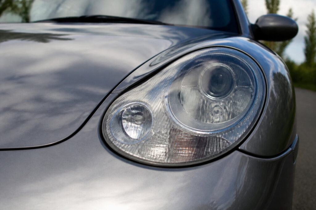 Gros plan sur le phare avant caractéristique d'une Porsche 996 grise sur une route en extérieur.